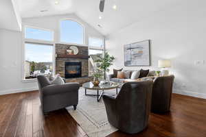 Living room with a high ceiling, ceiling fan, a stone fireplace, dark wood-style flooring, and recessed lighting