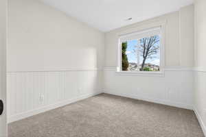 Empty room with carpet floors, wainscoting, and lofted ceiling