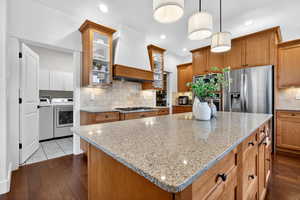 Kitchen with light stone counters, a center island, dark wood-type flooring, and glass insert cabinets