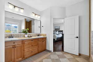 Ensuite bathroom featuring double vanity, decorative backsplash, and light tile patterned floors