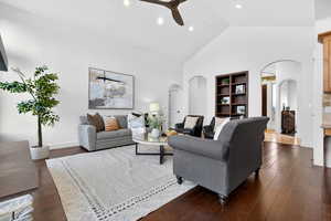 Living room with ceiling fan, vaulted ceiling, dark wood-style floors, arched walkways, and built in features