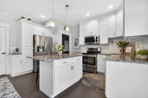 Kitchen with stainless steel appliances, dark stone countertops, white cabinetry, a breakfast bar area, and tasteful backsplash