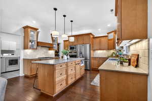 Kitchen with glass insert cabinets, light stone counters, stainless steel appliances, a center island, and wood finish cabinets