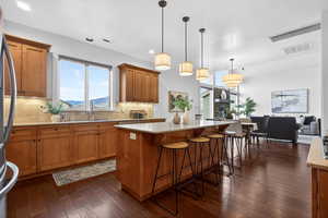 Kitchen featuring wood finish cabinets, light stone countertops, a center island, a breakfast bar area, and dark wood-style flooring