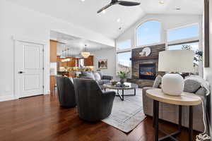 Living area with dark wood-style flooring, lofted ceiling, a stone fireplace, plenty of natural light, and ceiling fan