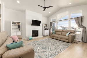 Living area with ceiling fan, recessed lighting, light wood-style flooring, lofted ceiling, and a glass covered fireplace