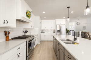 Dual tone kitchen featuring stainless steel appliances, hanging light fixtures, light wood finished floors, dual tone cabinets, and light stone countertops