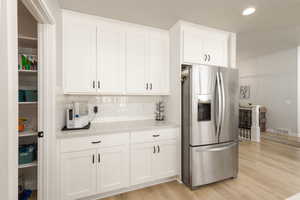 Kitchen with stainless steel fridge, white cabinetry, light wood-style flooring, recessed lighting, and backsplash