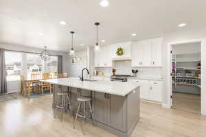 Two tone kitchen with dual tone cabinetry, a breakfast bar, an island with sink, light wood finished floors, and decorative light fixtures