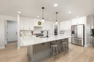 Two tone kitchen featuring stainless steel appliances, two tone cabinetry, a kitchen island with sink, a kitchen breakfast bar, and light wood finished floors