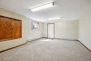 Spare room featuring a baseboard radiator, a textured ceiling, light colored carpet, and a baseboard heating unit