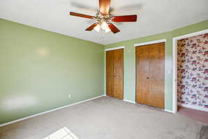 Unfurnished bedroom with two closets, light carpet, and ceiling fan