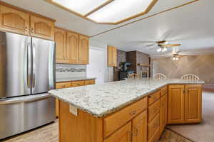 Kitchen with freestanding refrigerator, backsplash, ceiling fan, light stone counters, and light wood-type flooring