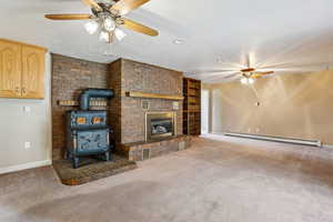 Unfurnished living room with a ceiling fan, a baseboard heating unit, a textured ceiling, carpet, and a wood stove
