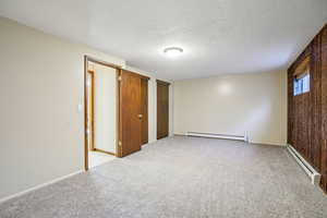 Unfurnished bedroom featuring a baseboard radiator, light carpet, a textured ceiling, a closet, and wood walls
