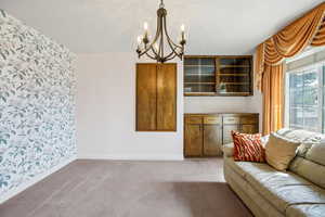 Living room with hanging lights, carpet, and wallpapered walls