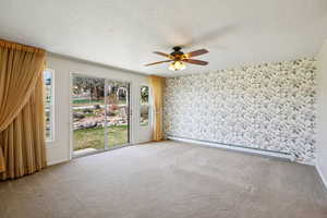 Empty room with a baseboard heating unit, a ceiling fan, carpet floors, wallpapered walls, and a textured ceiling