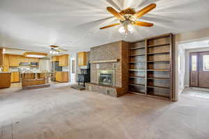 Unfurnished living room with a ceiling fan, a textured ceiling, light carpet, and a brick fireplace