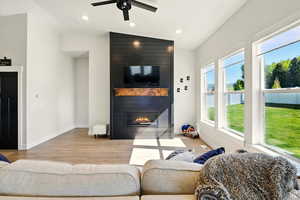 Living area with wood finished floors, a large fireplace, ceiling fan, vaulted ceiling, and large windows