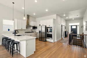Kitchen featuring stainless steel appliances, stainless steel chimney range hood, open floor plan, a kitchen bar, and a sink