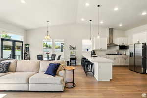 Kitchen featuring stainless steel appliances, stainless steel chimney range hood, open floor plan, a kitchen bar, and a sink
