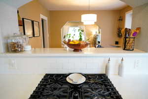 Kitchen view of black gas cooktop, light countertops, arched walkways, a textured wall, and hanging light fixtures