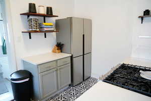 Kitchen featuring open shelves, gray cabinets, freestanding refrigerator, range with gas cooktop, and light tile patterned flooring