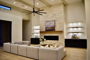 Living room with built in features, a high ceiling, light wood-type flooring, a stone fireplace, and ceiling fan