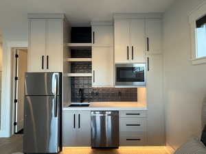 Kitchen featuring stainless steel appliances, open shelves, tasteful backsplash, light wood finished floors, and white cabinets