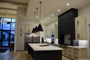 Two tone kitchen featuring two tone color scheme, light wood-style floors, built in appliances, a kitchen island with sink, and light stone countertops