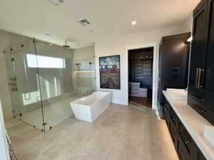 Bathroom with double vanity, a freestanding tub, a stall shower, a spacious closet, and recessed lighting