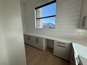 Kitchen view of built in desk, light wood finished floors, wood walls, and light stone counters