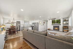 Living area with a glass covered fireplace, dark wood-style floors, ceiling fan, and a chandelier