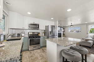 Two tone kitchen with two tone cabinetry, stainless steel appliances, a breakfast bar area, light stone countertops, and a kitchen island
