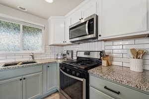 Kitchen with stainless steel appliances, light stone countertops, decorative backsplash, white cabinets, and recessed lighting