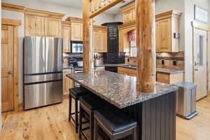 Kitchen with light wood finish cabinetry, stainless steel appliances, a breakfast bar area, tasteful backsplash, and light wood finished floors