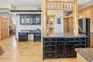 Two tone kitchen featuring two tone color scheme, freestanding refrigerator, light wood-type flooring, dark stone countertops, and a kitchen island