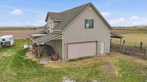 View of side of property featuring a view of countryside, an attached garage, roof with shingles, a mountain view, a driveway, RV parking, horse stalls and run.