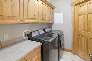 Laundry area with cabinet space, washing machine and clothes dryer, and light tile patterned floors