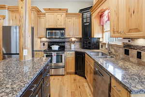 Two tone kitchen with stainless steel appliances, light wood-style flooring, dark stone counters, decorative backsplash, and dual tone cabinetry