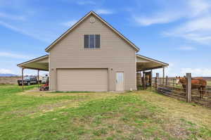 View of the front of the ADU/workshop behind the house with a carport, a wide pull-through 20cargarage, 3 horse stalls, a tack room, and a grazing area.