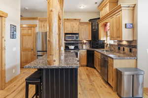 Kitchen with dark stone countertops, light wood-style floors, stainless steel appliances, and a kitchen breakfast bar