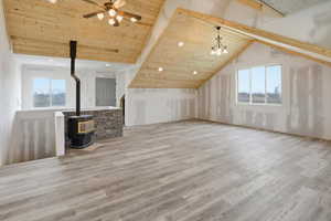 Unfurnished living room featuring a wood stove, a high wooden beamed ceiling, plenty of natural light, light wood-style floors, and ceiling fan