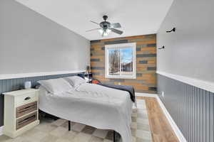 Bedroom featuring wooden walls, wainscoting, and ceiling fan