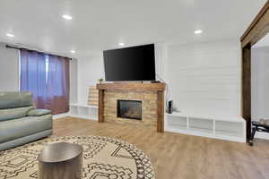 Living room featuring light wood-style flooring, a stone fireplace, and recessed lighting