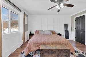 Bedroom with a decorative wall, wood finished floors, wainscoting, and a ceiling fan