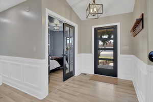 Entrance foyer featuring wainscoting, a decorative wall, french doors, a chandelier, and vaulted ceiling