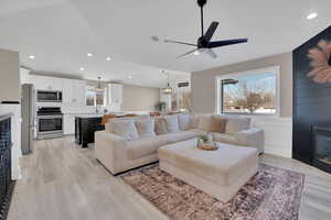 Living room featuring ceiling fan, a fireplace, light wood-style floors, recessed lighting, and wainscoting