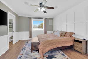 Bedroom with a decorative wall, a wainscoted wall, ornamental molding, light wood-style flooring, and ceiling fan
