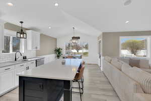 Dual tone kitchen with a center island, pendant lighting, dual tone cabinets, lofted ceiling, and a kitchen breakfast bar